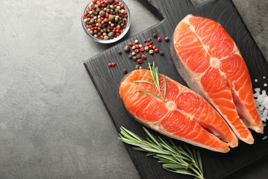 Photo of Seafood. Raw salmon steaks, rosemary and spices on grey table, flat lay. Space for text