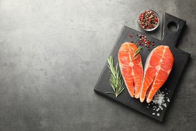 Photo of Seafood. Raw salmon steaks, rosemary and spices on grey table, flat lay. Space for text