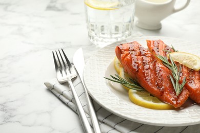 Photo of Seafood. Tasty grilled salmon served with cutlery, rosemary and lemon on white marble table, closeup. Space for text