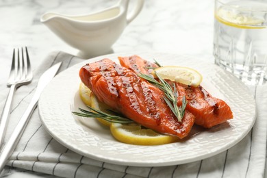 Photo of Seafood. Tasty grilled salmon served with cutlery, rosemary and lemon on white table, closeup