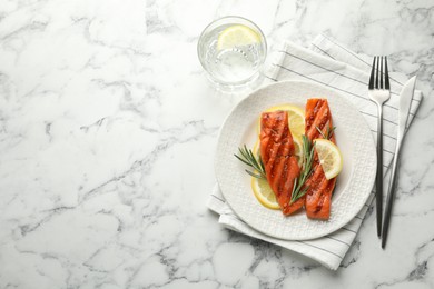 Photo of Seafood. Tasty grilled salmon served with water, cutlery, rosemary and lemon on white marble table, flat lay. Space for text