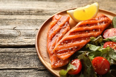 Photo of Seafood. Tasty grilled salmon served with salad and lemon on wooden table, closeup. Space for text