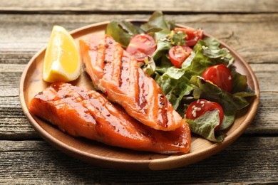 Photo of Seafood. Tasty grilled salmon served with salad and lemon on wooden table, closeup