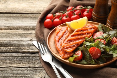 Photo of Seafood. Tasty grilled salmon served with cutlery, salad and lemon on wooden table, closeup. Space for text