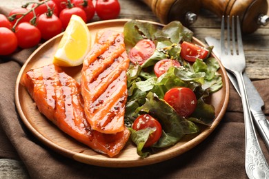 Photo of Seafood. Tasty grilled salmon served with cutlery, salad and lemon on wooden table, closeup