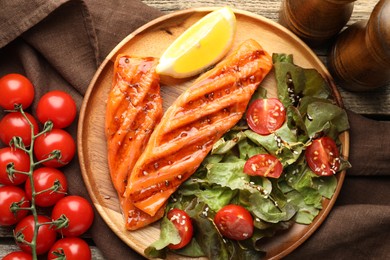Photo of Tasty grilled salmon served with salad, tomatoes and lemon on wooden table, flat lay
