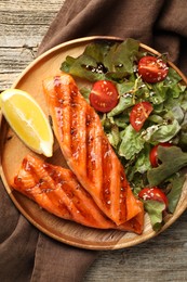 Photo of Tasty grilled salmon served with salad and lemon on wooden table, top view
