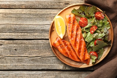Photo of Tasty grilled salmon served with salad and lemon on wooden table, top view. Space for text