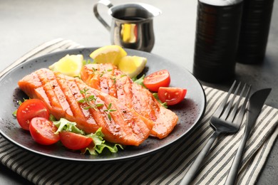 Photo of Tasty grilled salmon served with lettuce, tomatoes and lemon on grey table, closeup
