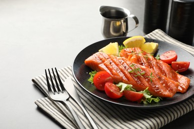 Photo of Tasty grilled salmon served with lettuce, tomatoes and lemon on grey table, closeup. Space for text