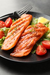 Photo of Tasty grilled salmon served with lettuce, tomatoes and lemon on grey table, closeup