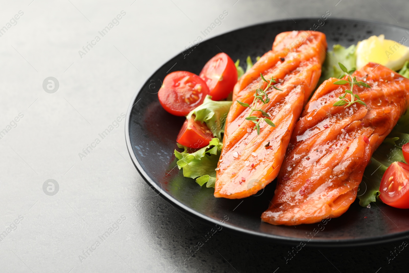 Tasty grilled salmon served with lettuce, tomatoes and lemon on grey table, closeup. Space for text Photo of Tasty grilled salmon served with lettuce, tomatoes and lemon on grey table, closeup. Space for text