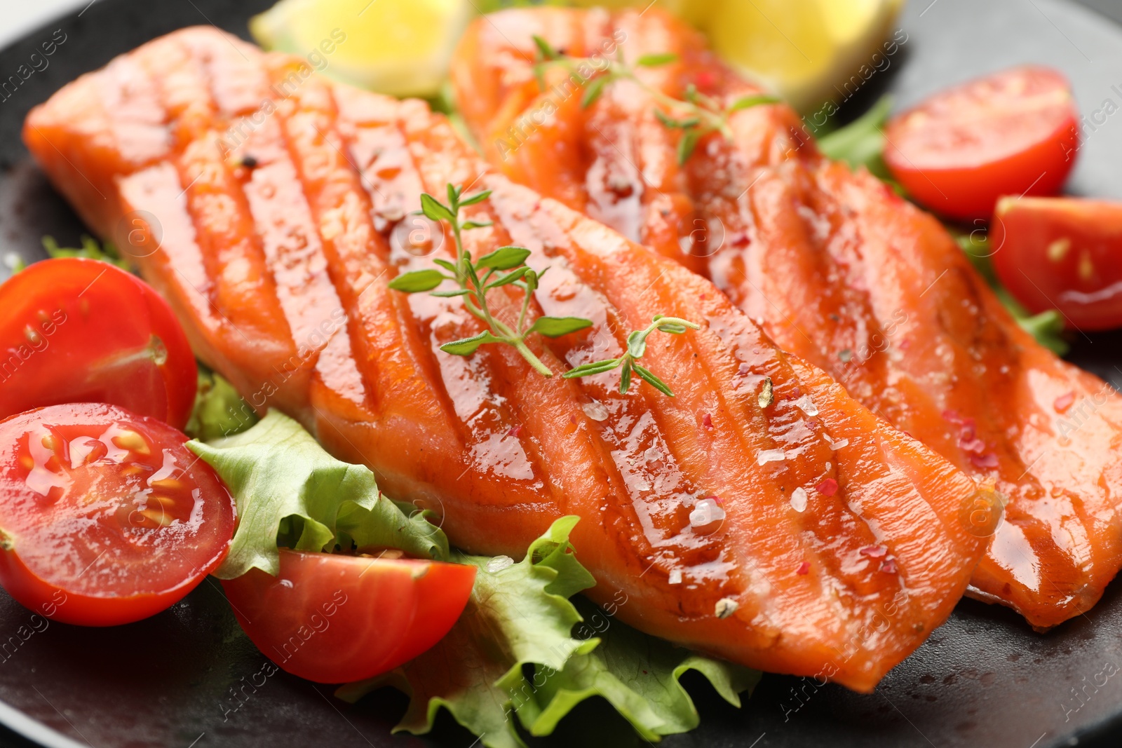 Tasty grilled salmon served with lettuce, tomatoes and lemon on table, closeup Photo of Tasty grilled salmon served with lettuce, tomatoes and lemon on table, closeup