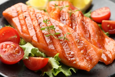 Photo of Tasty grilled salmon served with lettuce, tomatoes and lemon on table, closeup