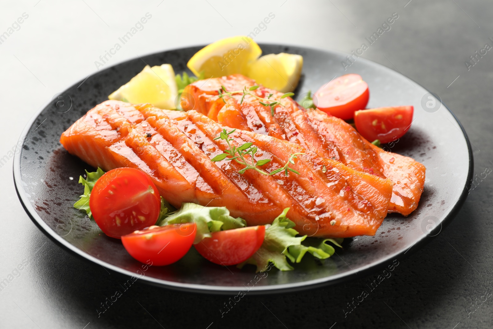 Tasty grilled salmon served with lettuce, tomatoes and lemon on grey table, closeup Photo of Tasty grilled salmon served with lettuce, tomatoes and lemon on grey table, closeup