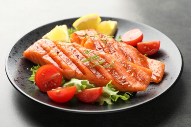 Photo of Tasty grilled salmon served with lettuce, tomatoes and lemon on grey table, closeup