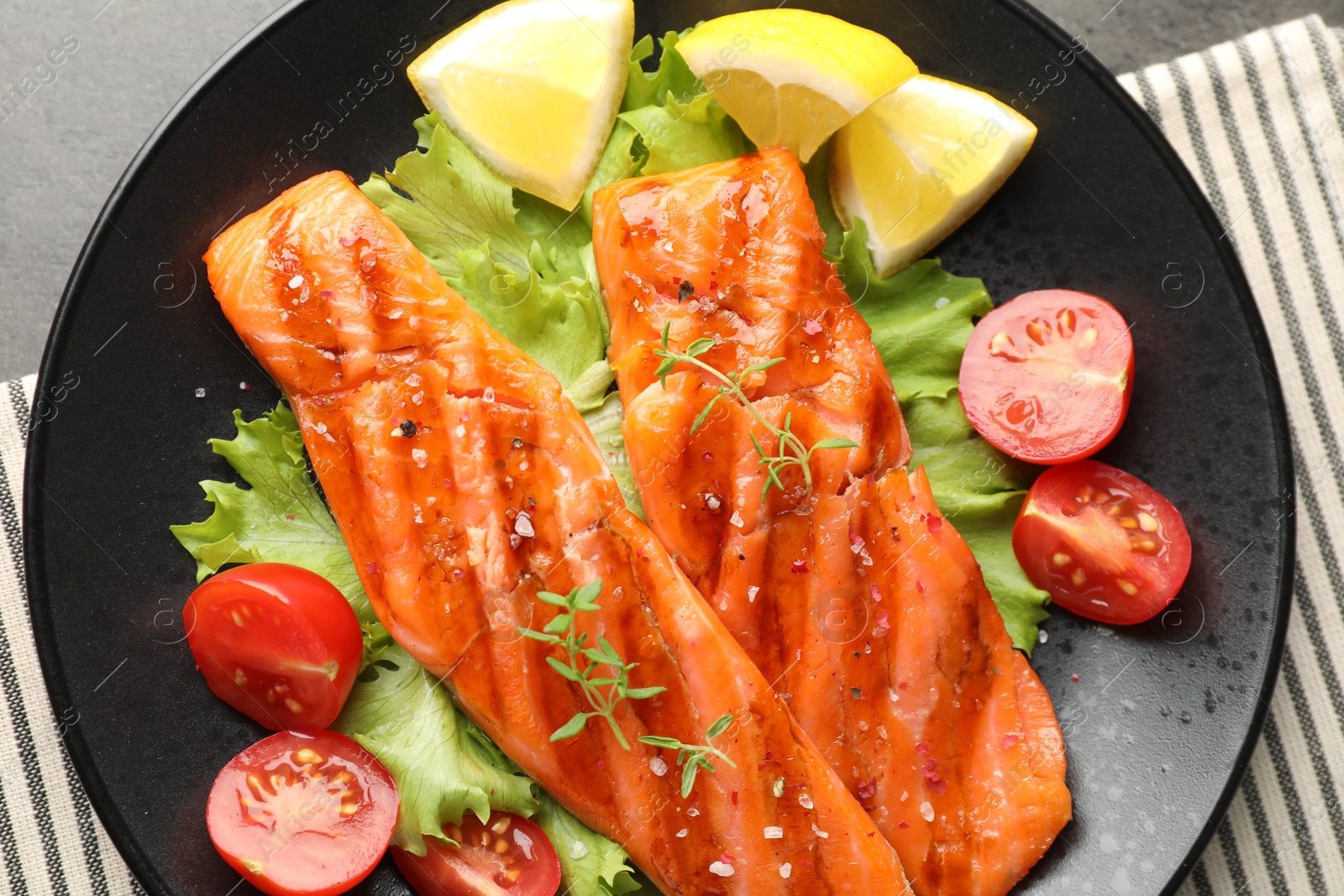 Tasty grilled salmon served with lettuce, tomatoes and lemon on grey table, top view Photo of Tasty grilled salmon served with lettuce, tomatoes and lemon on grey table, top view