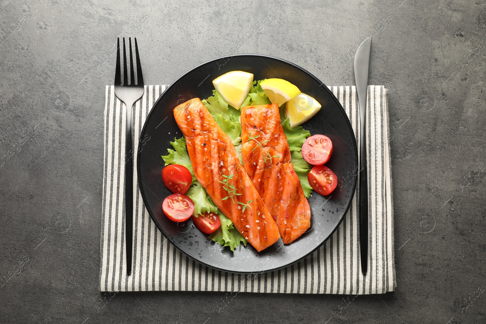 Tasty grilled salmon served with cutlery, lettuce, tomatoes and lemon on grey table, top view Photo of Tasty grilled salmon served with cutlery, lettuce, tomatoes and lemon on grey table, top view