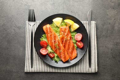 Photo of Tasty grilled salmon served with cutlery, lettuce, tomatoes and lemon on grey table, top view