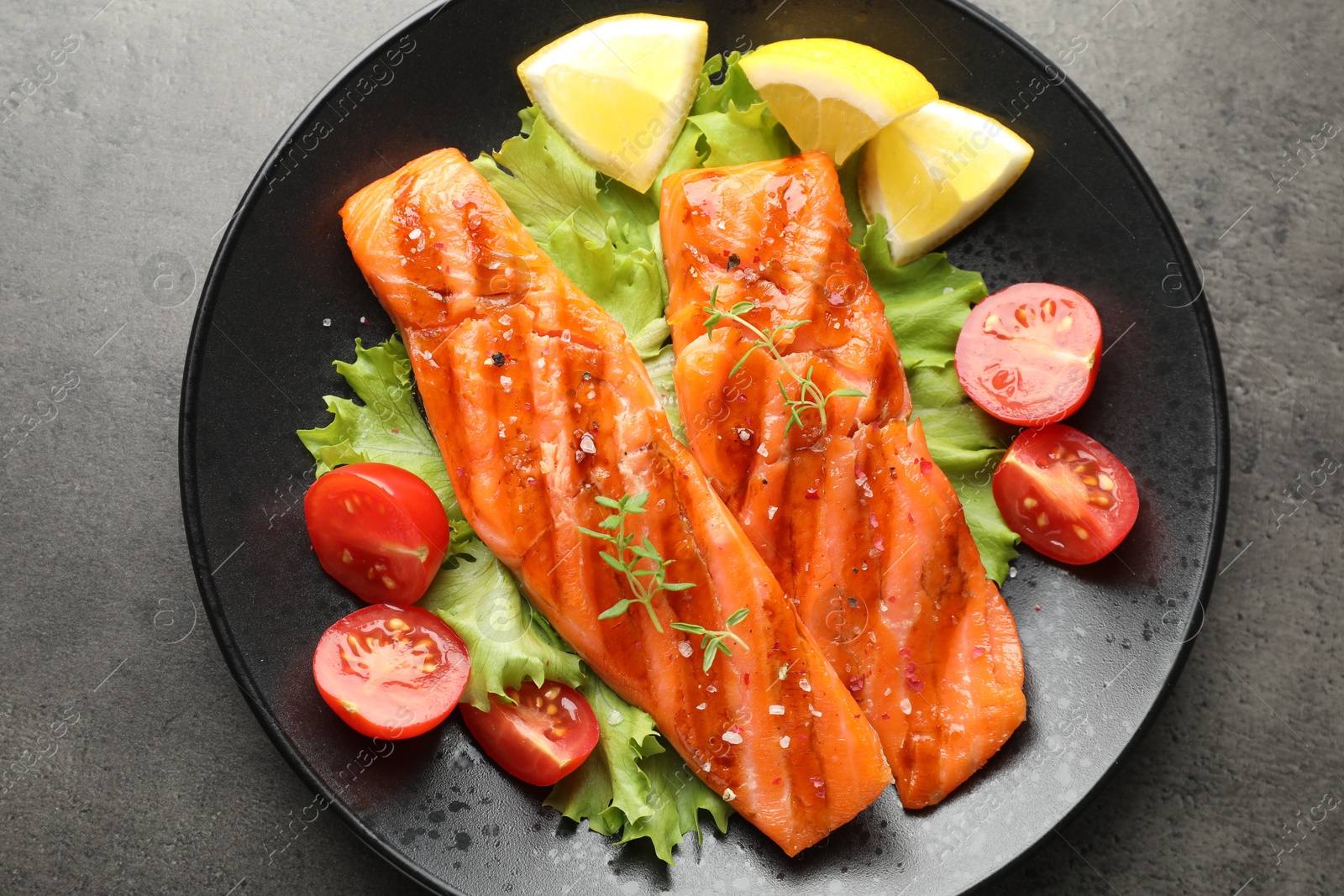 Tasty grilled salmon served with lettuce, tomatoes and lemon on grey table, top view Photo of Tasty grilled salmon served with lettuce, tomatoes and lemon on grey table, top view