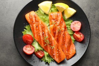 Photo of Tasty grilled salmon served with lettuce, tomatoes and lemon on grey table, top view