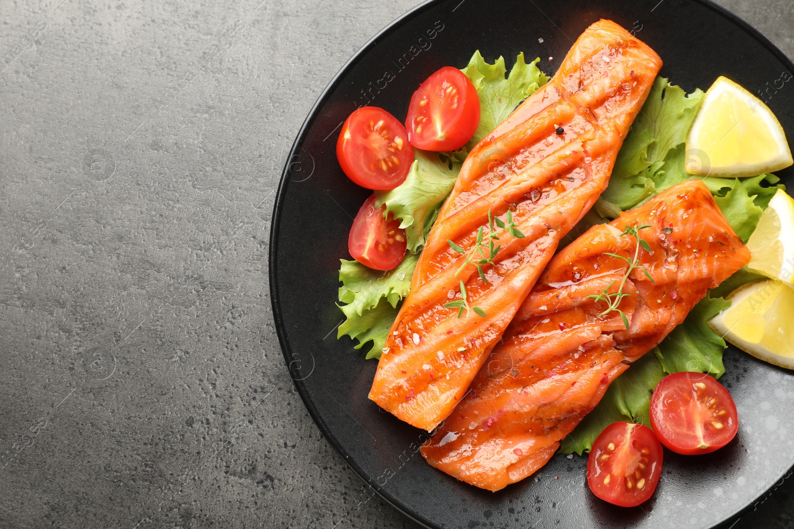 Tasty grilled salmon served with lettuce, tomatoes and lemon on grey table, top view. Space for text Photo of Tasty grilled salmon served with lettuce, tomatoes and lemon on grey table, top view. Space for text