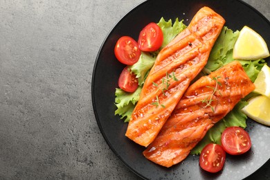Photo of Tasty grilled salmon served with lettuce, tomatoes and lemon on grey table, top view. Space for text
