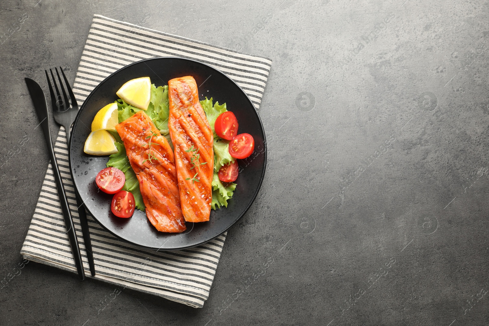 Tasty grilled salmon served with cutlery, lettuce, tomatoes and lemon on grey table, top view. Space for text Photo of Tasty grilled salmon served with cutlery, lettuce, tomatoes and lemon on grey table, top view. Space for text
