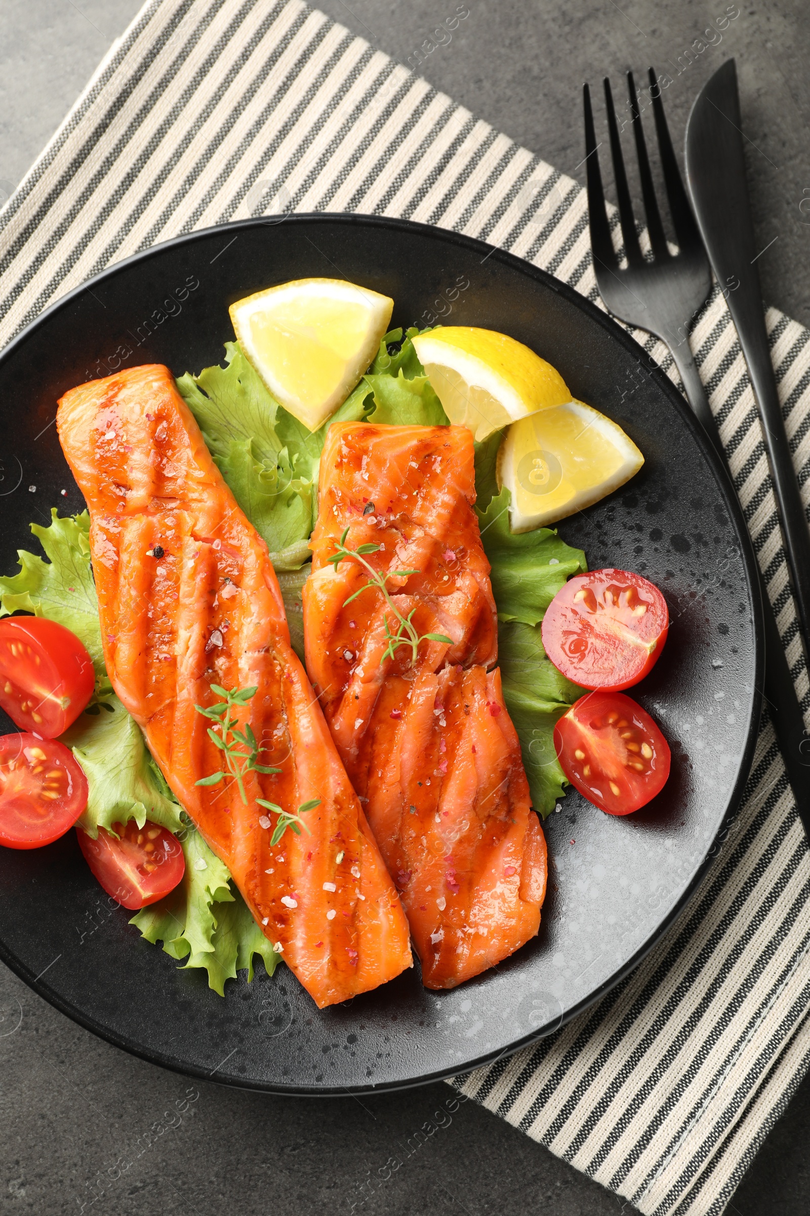 Tasty grilled salmon served with cutlery, lettuce, tomatoes and lemon on grey table, top view Photo of Tasty grilled salmon served with cutlery, lettuce, tomatoes and lemon on grey table, top view