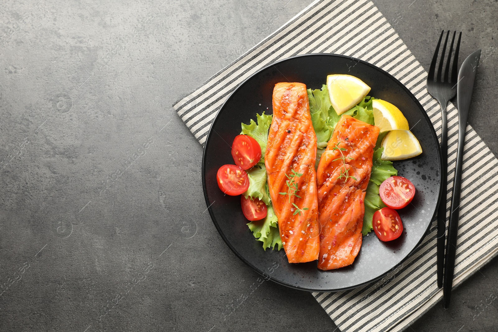 Tasty grilled salmon served with cutlery, lettuce, tomatoes and lemon on grey table, top view. Space for text Photo of Tasty grilled salmon served with cutlery, lettuce, tomatoes and lemon on grey table, top view. Space for text