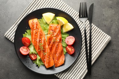 Photo of Tasty grilled salmon served with cutlery, lettuce, tomatoes and lemon on grey table, top view