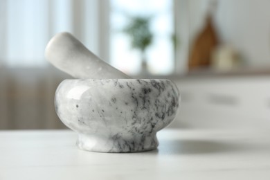 Photo of Mortar and pestle on white marble table in kitchen, closeup