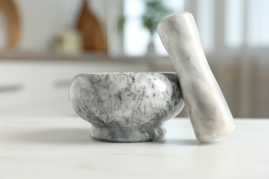 Photo of Mortar and pestle on white marble table in kitchen, closeup