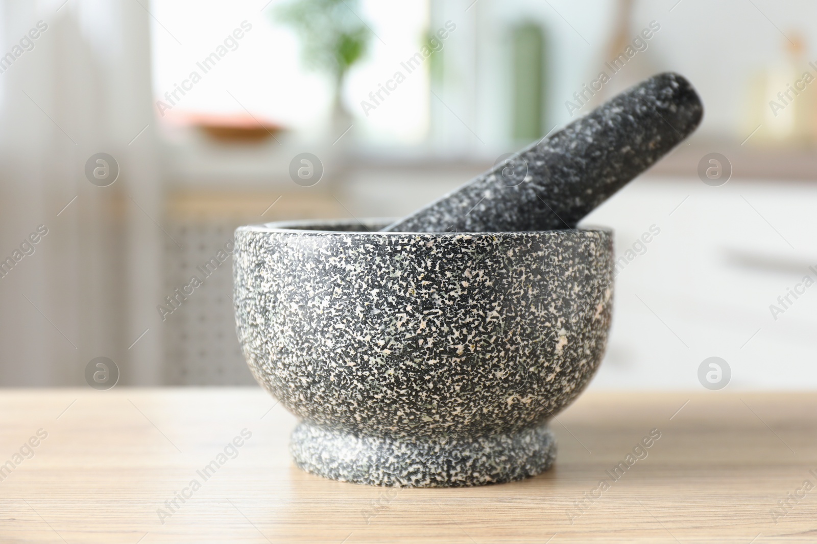 Stone mortar and pestle on wooden table in kitchen Photo of Stone mortar and pestle on wooden table in kitchen