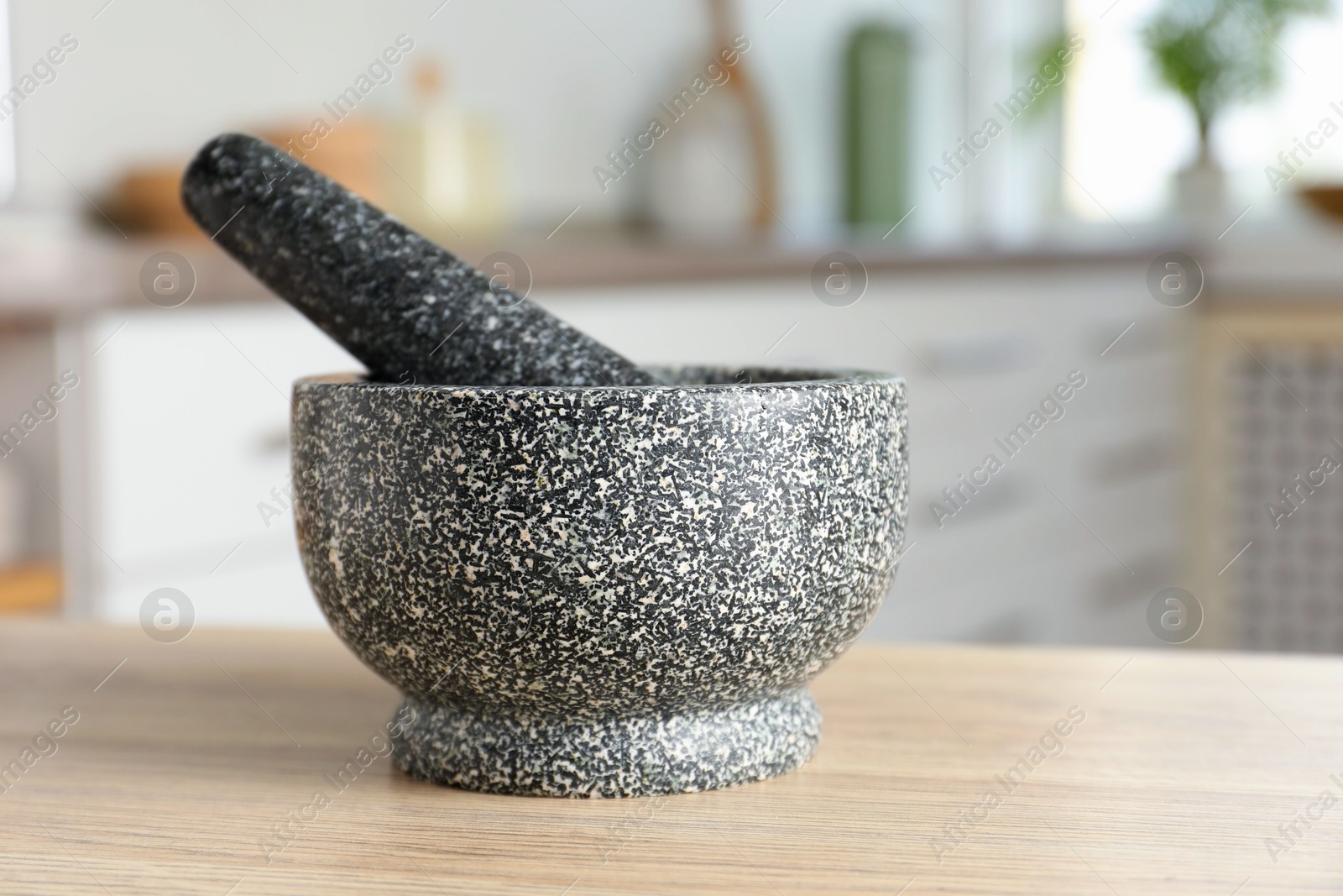 Stone mortar and pestle on wooden table in kitchen Photo of Stone mortar and pestle on wooden table in kitchen