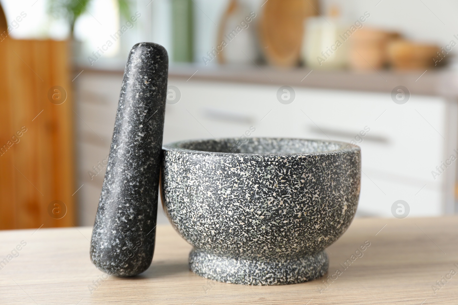 Stone mortar and pestle on wooden table in kitchen Photo of Stone mortar and pestle on wooden table in kitchen