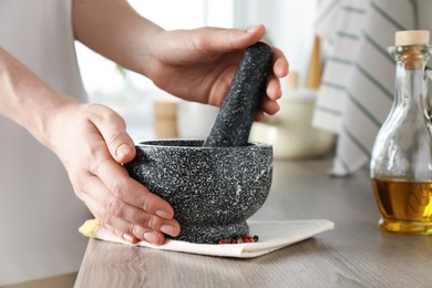 Photo of Woman with mortar and pestle at wooden table in kitchen, closeup