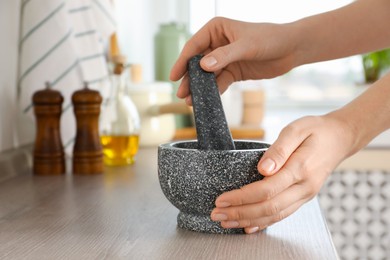 Photo of Woman with mortar and pestle at wooden table in kitchen, closeup