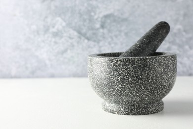 Photo of Stone mortar and pestle on white table, closeup. Space for text