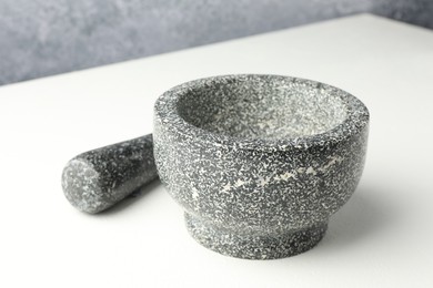 Photo of Stone mortar and pestle on white table, closeup