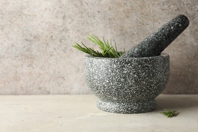 Photo of Stone mortar with rosemary and pestle on light table, closeup. Space for text
