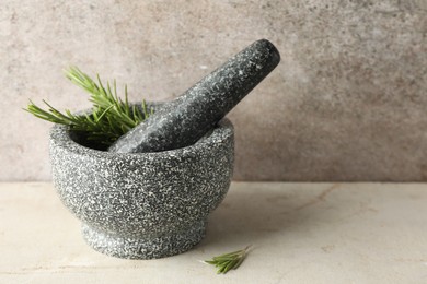 Photo of Stone mortar with rosemary and pestle on light table, closeup. Space for text