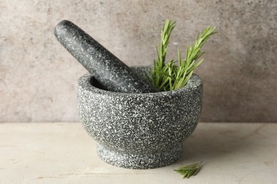 Photo of Stone mortar with rosemary and pestle on light table, closeup