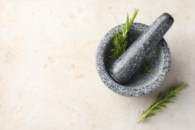 Photo of Stone mortar with rosemary and pestle on light table, top view. Space for text