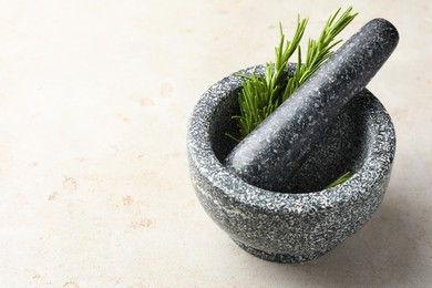 Photo of Stone mortar with rosemary and pestle on light table, closeup. Space for text