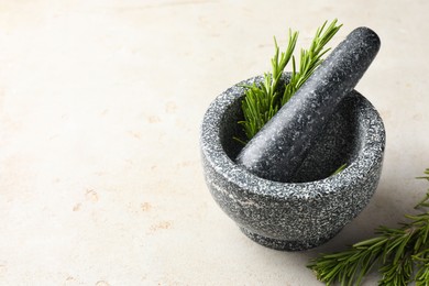 Photo of Stone mortar with rosemary and pestle on light table, closeup. Space for text
