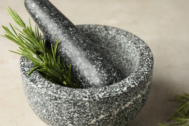 Photo of Stone mortar with rosemary and pestle on light table, closeup