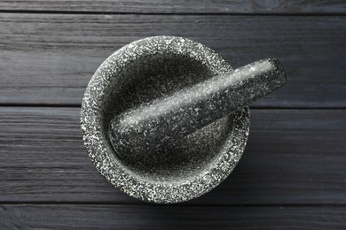 Photo of Stone mortar and pestle on black wooden table, top view