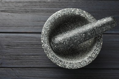 Photo of Stone mortar and pestle on black wooden table, top view