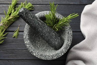Photo of Stone mortar with rosemary and pestle on black wooden table, flat lay